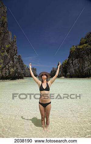 A Woman Tourist Wearing A Sun Hat And Bikini Stands With Arms Raised In The Clear Waters Of Matinloc Island Near El Nido And Corong Corong; Bacuit Archipelago; Palawan Philippines View Large Photo Image Stock Image - A Woman Tourist Wearing A Sun Hat And Bikini Stands With Arms Raised In The Clear Waters Of Matinloc Island Near El Nido And Corong Corong; Bacuit Archipelago; Palawan Philippines. Fotosearch