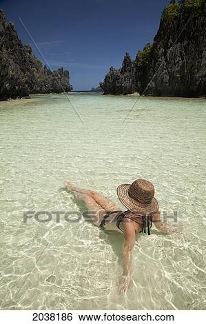 Stock Photograph - A Woman Tourist Wearing A Sun Hat And Bikini Relaxes In The Clear Waters Of Matinloc Island Near El Nido And Corong Corong; Bacuit Archipelago Palawan Philippines. Fotosearch