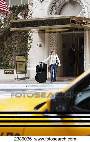 A woman waits with her luggage for a ride on the street outside a hotel; California, United States of America View Large Photo Image Stock Photograph - A woman waits with her luggage for a ride on the street outside a hotel; California, United States of America. Fotosearch