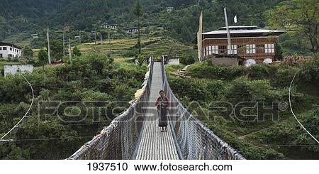 Stock Image - A Woman Walking On A Suspension Bridge; Punakha District Bhutan. Fotosearch