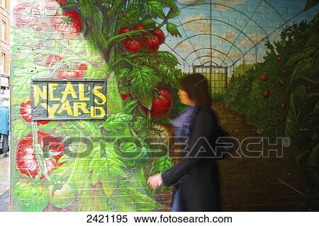 Stock Photography - A woman walks by a colourful mural painted on a brick wall, Covent Garden; London, England. Fotosearch
