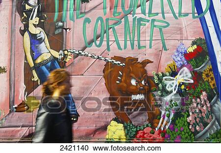 Stock Image - A woman walks by a wall painted with a colourful mural, Portobello Road Market; London, England. Fotosearch