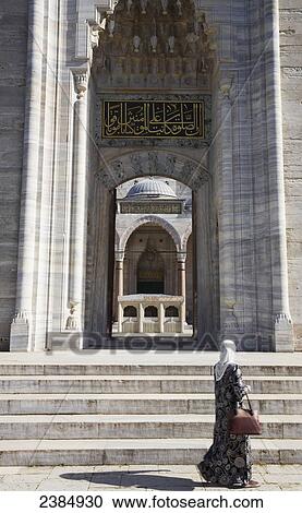 Stock Image - A woman walks by the entrance of an islamic mosque; Istanbul, Turkey. Fotosearch