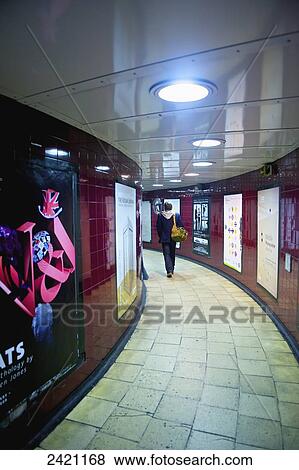 Stock Photo - A woman walks down a curved corridor lined with advertisements; London, England. Fotosearch