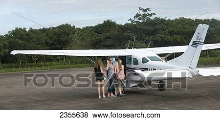 Stock Photo - A Woman Waves Goodbye As She And Two Daughters Board A Plane On A Tarmac; La Lima, Cortes, Honduras. Fotosearch