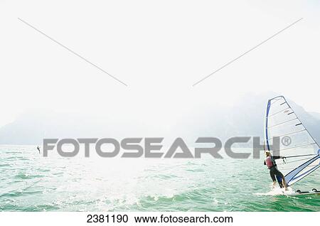 Stock Image - A woman windsurfing on Lake Garda; Riva del Garda, Trento, Northern Italy. Fotosearch