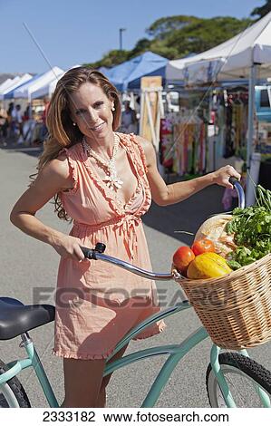 Stock Image - A woman with her bike and a basket full of fresh produce at an outdoor market; Honolulu, Oahu, Hawaii, United States of America. Fotosearch