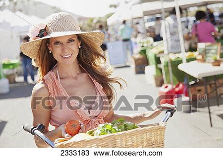 Stock Image - A woman with her bike and a basket full of fresh produce at an outdoor market; Honolulu, Oahu, Hawaii, United States of America. Fotosearch
