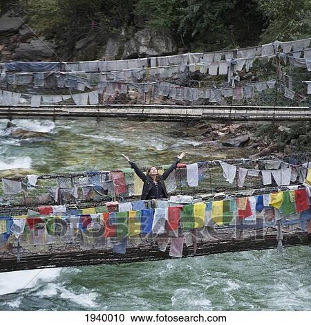 A Woman With Raised Arms On An Iron Suspension Bridge Lined With Prayer Flags; Tamchhog Lhakhang Bhutan View Large Photo Image Stock Image - A Woman With Raised Arms On An Iron Suspension Bridge Lined With Prayer Flags; Tamchhog Lhakhang Bhutan. Fotosearch