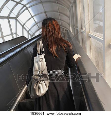 Stock Image - A Woman With Red Hair On An Escalator; Tianjin China. Fotosearch