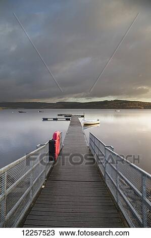 A wooden dock with white metal railing leading out to a tranquil lake with clouds at sunset; Kielder, Northumberland, England View Large Photo Image Stock Image - A wooden dock with white metal railing leading out to a tranquil lake with clouds at sunset; Kielder, Northumberland, England. Fotosearch