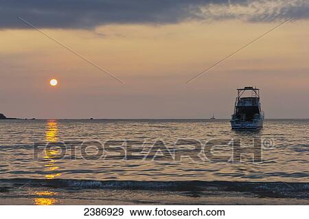 Stock Photo - A yacht sits in the tranquil ocean water at sunset off Waikoloa beach in Anaehoomalu Bay; Island of Hawaii, Hawaii, United States of America. Fotosearch