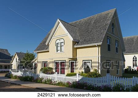 Stock Image - A yellow house with a white picket fence and blue sky; Green Gables, Prince Edward Island, Canada. Fotosearch
