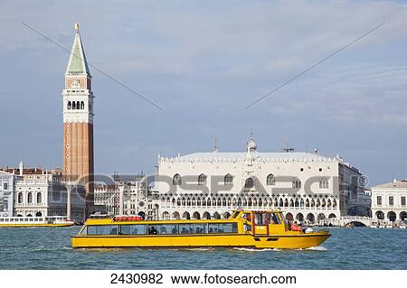Stock Image - A yellow tour boat in the water with a view of Venice from San Giorgio Maggiore; Venice, Italy. Fotosearch