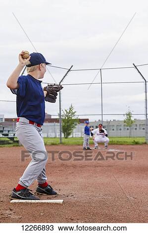 Stock Image - A young boy in his baseball uniform prepares to throw a pitch to his brother at bat; Fort McMurray, Alberta, Canada. Fotosearch