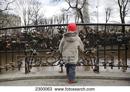 Stock Image - A young boy plays with locks attached to Love Lock Bridge in Baste Kalns Park. It is good luck and tradition for grooms to carry their brides over the 7 bridges in Riga and attach their lock to seal their love to one, Riga, Latvia.. Fotosearch