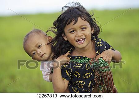 A young Bunong girl carrying her baby sister on her back; Mondulkiri, Cambodia View Large Photo Image Stock Photo - A young Bunong girl carrying her baby sister on her back; Mondulkiri, Cambodia. Fotosearch