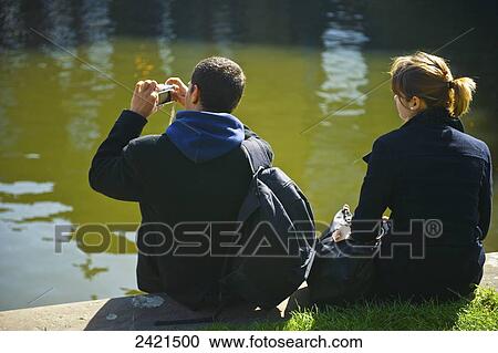 A young couple sits by the water's edge taking pictures; London, England View Large Photo Image Stock Image - A young couple sits by the water's edge taking pictures; London, England. Fotosearch