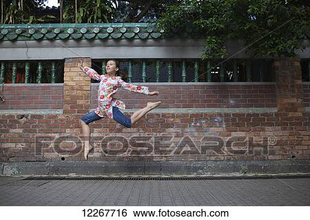 Stock Photograph - A young girl jumping in mid-air in an urban area; Hong Kong. Fotosearch