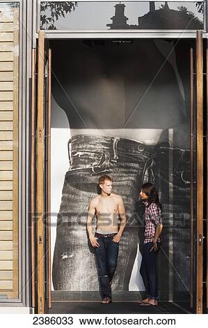 A young man and woman stand talking inside a retail store with a denim jean advertisement behind them; California, United States of America View Large Photo Image Stock Image - A young man and woman stand talking inside a retail store with a denim jean advertisement behind them; California, United States of America. Fotosearch