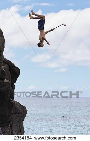 Picture - A young man enjoys a 30 foot high jump at da big rock in Waimea Bay; North Shore, Oahu, Hawaii, United States of America. Fotosearch