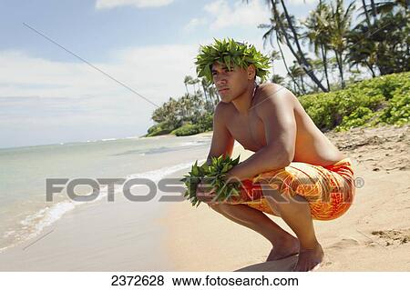 Stock Photo - A young man on the beach wearing a green leaf crown and bracelets; Honolulu, Oahu, Hawaii, United States of America. Fotosearch