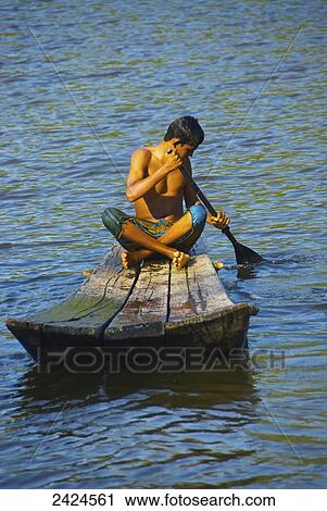 Stock Image - A young man paddles a wooden raft; Ulpotha, Embogama, Sri Lanka. Fotosearch