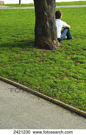 A young man sits by a tree in an urban park, Shoreditch; London, England View Large Photo Image Stock Image - A young man sits by a tree in an urban park, Shoreditch; London, England. Fotosearch