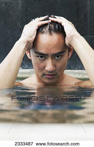 Stock Photo - A young man sitting by the edge of the pool holding his head in his hands; Honolulu, Oahu, Hawaii, United States of America. Fotosearch