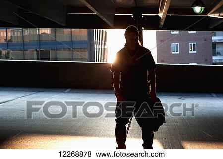 A young man stands in an elevated parking lot backlit by the setting sun in an urban area; Burlington, Vermont, United States of America View Large Photo Image Stock Photo - A young man stands in an elevated parking lot backlit by the setting sun in an urban area; Burlington, Vermont, United States of America. Fotosearch