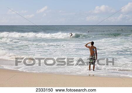 Stock Image - A young surfer checks out the incoming waves; Oahu, Hawaii, United States of America. Fotosearch