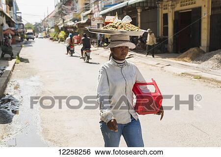 Stock Photograph - A young woman carrying her goods on her head in Central Market; Battambang, Cambodia. Fotosearch