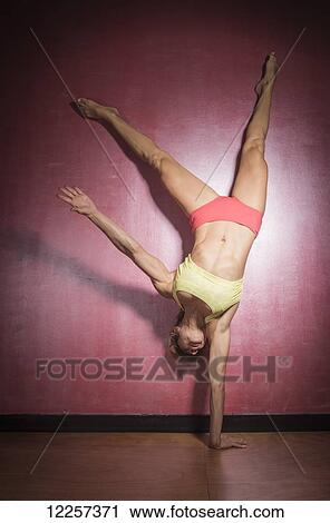 Stock Image - A young woman does a handstand balancing on one hand against a red wall; Tarifa, Cadiz, Andalusia, Spain. Fotosearch