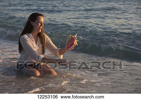 A young woman finds a seashell in the ocean at sunset; Nokomis, Florida, United States of America View Large Photo Image Stock Photograph - A young woman finds a seashell in the ocean at sunset; Nokomis, Florida, United States of America. Fotosearch