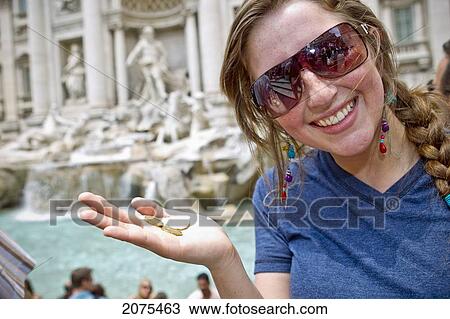 Stock Image - A Young Woman Holds Three Coins Beside Trevi Fountain; Rome Italy. Fotosearch