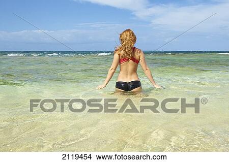 A young woman in a bikini enters the ocean water; Wailua, Hawaii, United States of America View Large Photo Image Picture - A young woman in a bikini enters the ocean water; Wailua, Hawaii, United States of America. Fotosearch