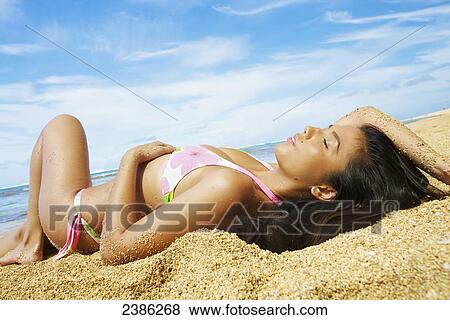 A young woman in a bikini laying on the sand; Hawaii, United States of America View Large Photo Image Stock Photo - A young woman in a bikini laying on the sand; Hawaii, United States of America. Fotosearch