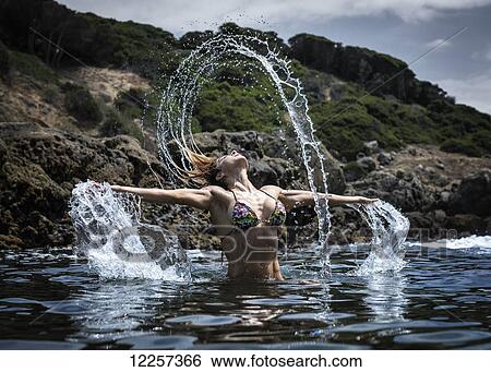 A young woman in a bikini splashing water along the water's edge; Tarifa, Cadiz, Andalusia, Spain View Large Photo Image Stock Photograph - A young woman in a bikini splashing water along the water's edge; Tarifa, Cadiz, Andalusia, Spain. Fotosearch