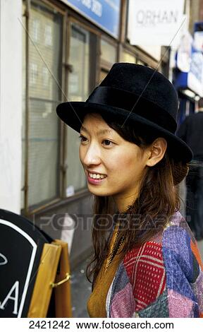 Stock Image - A young woman in a colourful shirt and black hat, Shoreditch; London, England. Fotosearch