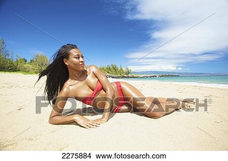 Picture - A young woman in a red bikini lays on a sandy beach; Maui, Hawaii, United States of America. Fotosearch
