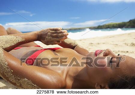 Stock Photo - A young woman in a red bikini lays on a sandy beach at the water's edge; Maui, Hawaii, United States of America. Fotosearch