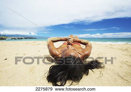 A young woman in a red bikini lays on a sandy beach at the water's edge; Maui, Hawaii, United States of America View Large Photo Image Stock Photo - A young woman in a red bikini lays on a sandy beach at the water's edge; Maui, Hawaii, United States of America. Fotosearch