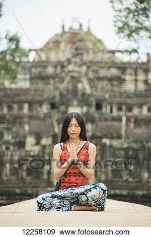 A young woman in meditation on Baphuon Temple is just next to Bayon Wat, built in Eleventh Century by Udayadityavarman II dedicated to the Hindu God Shiva, Angkor; Siem Reap, Cambodia View Large Photo Image Stock Photo - A young woman in meditation on Baphuon Temple is just next to Bayon Wat, built in Eleventh Century by Udayadityavarman II dedicated to the Hindu God Shiva, Angkor; Siem Reap, Cambodia. Fotosearch