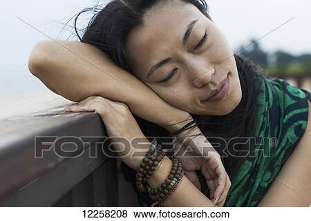 Stock Photo - A young woman lays her head against a wooden railing at the beach; Jincheng, Kinmen, Taiwan. Fotosearch