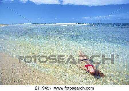 Stock Photo - A young woman lays in the shallow ocean water; Wailua, Hawaii, United States of America. Fotosearch