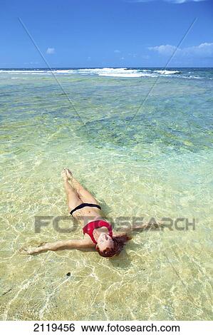 Stock Photograph - A young woman lays in the shallow ocean water; Wailua, Hawaii, United States of America. Fotosearch