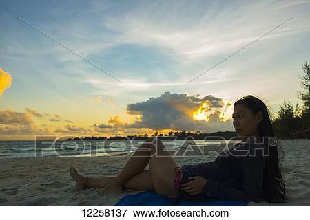 Stock Photo - A young woman lays posing on Sokha Beach at sunset; Sihanoukville, Cambodia. Fotosearch