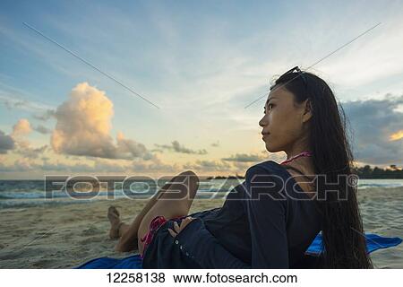 Stock Photo - A young woman lays posing on Sokha Beach at sunset; Sihanoukville, Cambodia. Fotosearch