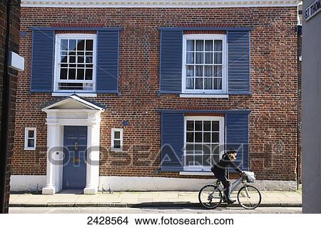 A young woman on a bicycle rides by a house with blue shutters and blue door; Winchester, Hampshire, England View Large Photo Image Picture - A young woman on a bicycle rides by a house with blue shutters and blue door; Winchester, Hampshire, England. Fotosearch