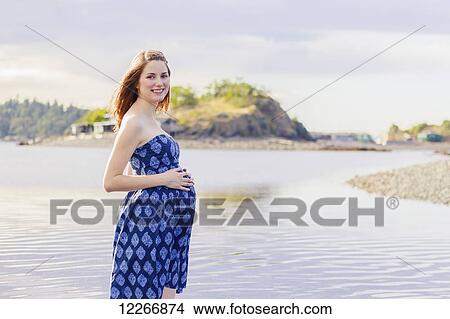 A young woman poses with a smile for a pregnancy maternity portrait on a beach at the ocean; Nanaimo, British Columbia, Canada View Large Photo Image Picture - A young woman poses with a smile for a pregnancy maternity portrait on a beach at the ocean; Nanaimo, British Columbia, Canada. Fotosearch